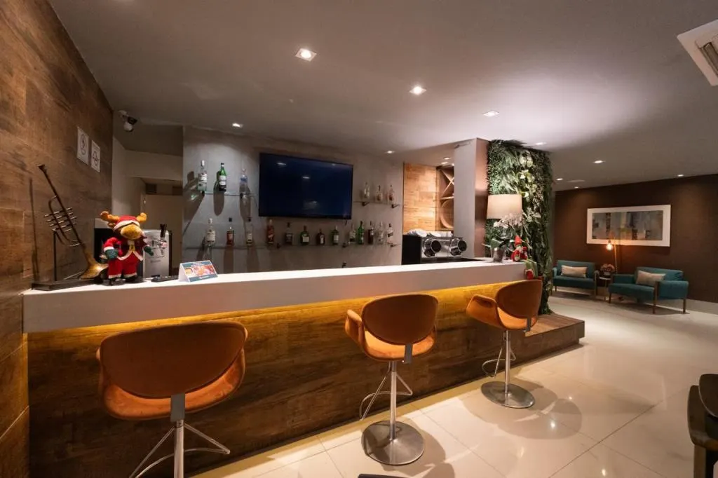Bar do Hotel Heritage, com balcão iluminado, banquetas e jardim vertical