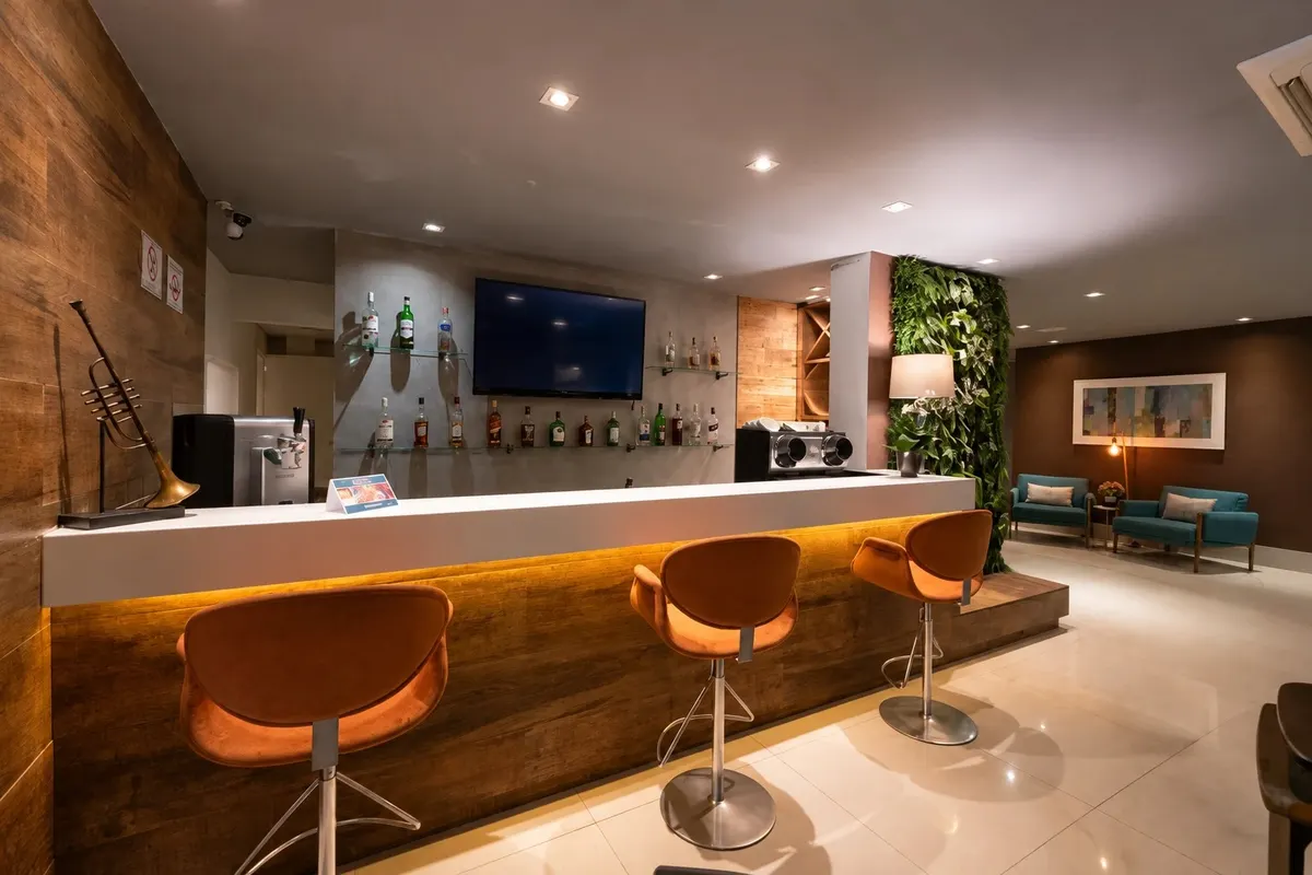 Bar do Hotel Heritage, com balcão iluminado, banquetas e jardim vertical