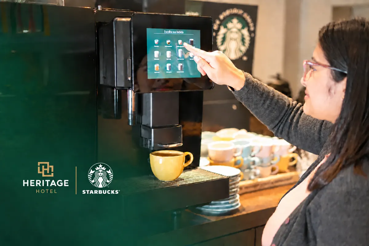 Hóspede escolhendo a bebida na máquina de café Starbucks do salão do café da manhã, com as marcas Heritage e Starbucks
